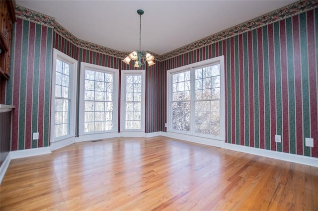 unfurnished room featuring visible vents, wood finished floors, a chandelier, baseboards, and wallpapered walls