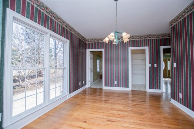 unfurnished dining area with baseboards, an inviting chandelier, wood finished floors, and wallpapered walls