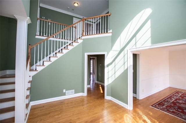 stairway with baseboards, visible vents, a towering ceiling, ornamental molding, and wood finished floors