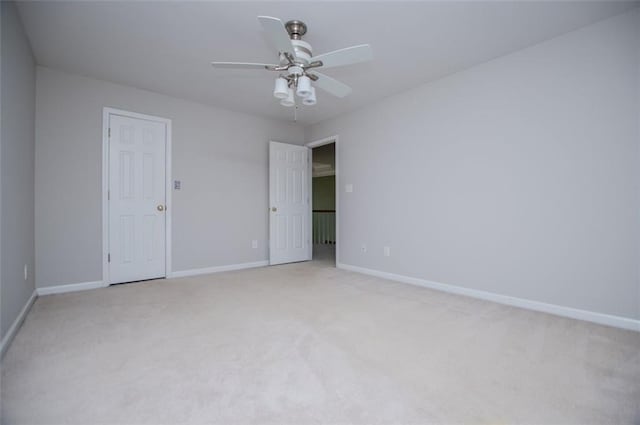 empty room featuring a ceiling fan, light colored carpet, and baseboards