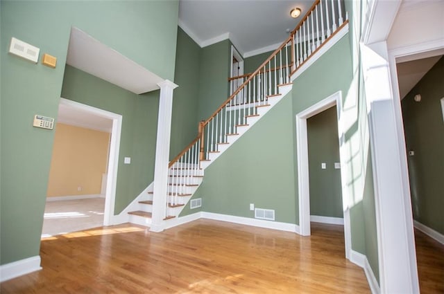 stairs featuring visible vents, crown molding, a towering ceiling, and wood finished floors