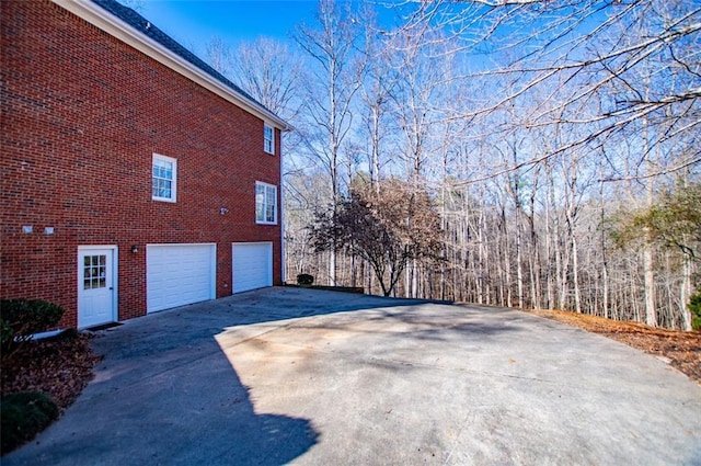 view of home's exterior with driveway, brick siding, and an attached garage