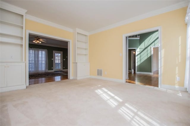 unfurnished living room featuring built in shelves, visible vents, ornamental molding, carpet flooring, and baseboards