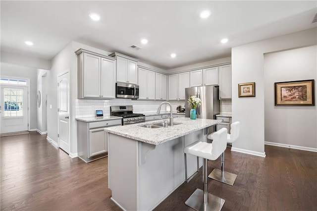 kitchen with light stone countertops, a kitchen bar, stainless steel appliances, sink, and a center island with sink