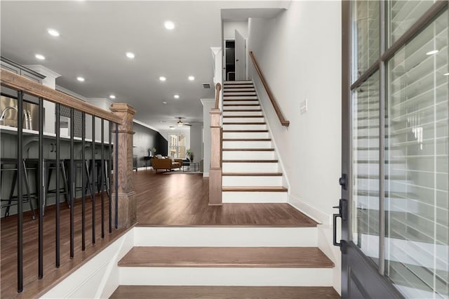 staircase with wood finished floors, baseboards, recessed lighting, ceiling fan, and ornamental molding