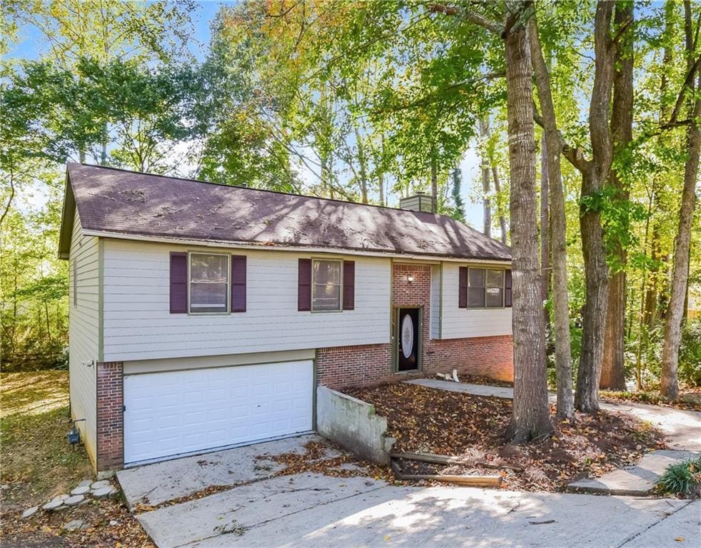 bi-level home with brick siding, a garage, a chimney, and concrete driveway