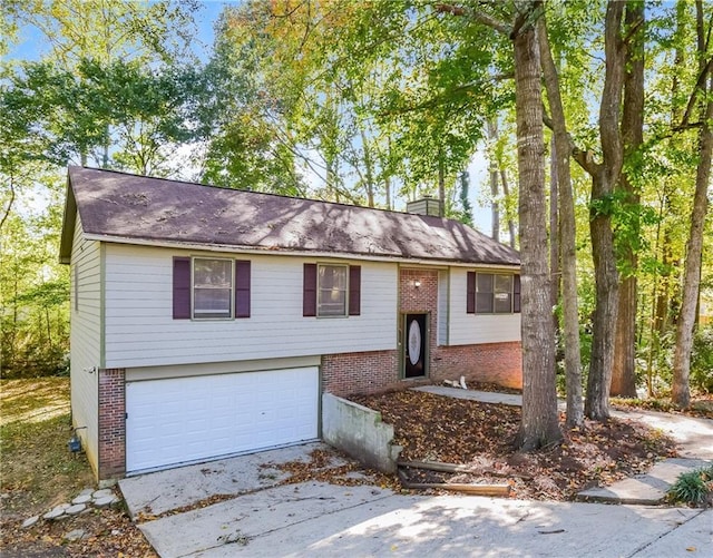 bi-level home with brick siding, a garage, a chimney, and concrete driveway
