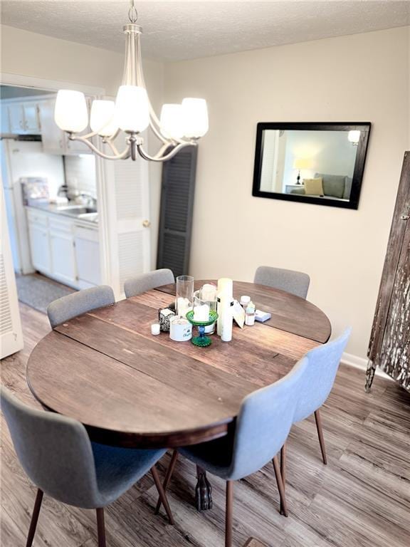 dining area with a notable chandelier, wood finished floors, baseboards, and a textured ceiling