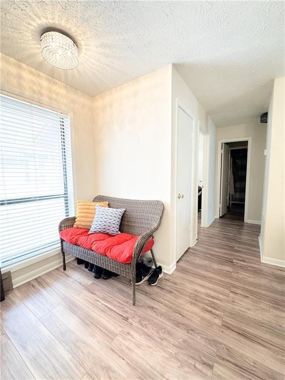 living area featuring baseboards, light wood-type flooring, and a textured ceiling