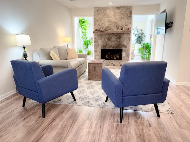 living room featuring light wood-style flooring, a fireplace, baseboards, and a healthy amount of sunlight