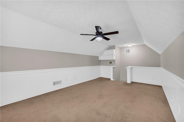 additional living space with ceiling fan, lofted ceiling, carpet flooring, and a textured ceiling