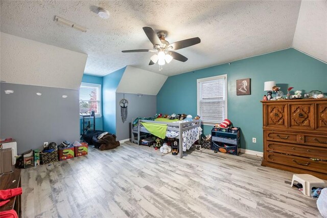 bedroom featuring lofted ceiling, a textured ceiling, light wood-type flooring, and ceiling fan