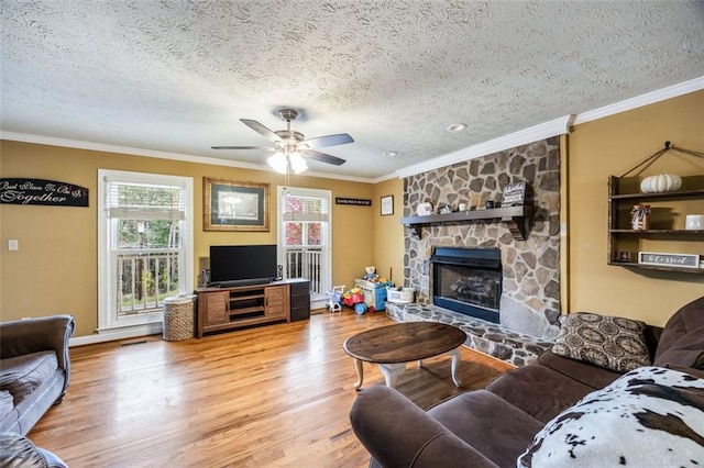 living room with a stone fireplace, hardwood / wood-style floors, crown molding, a textured ceiling, and ceiling fan