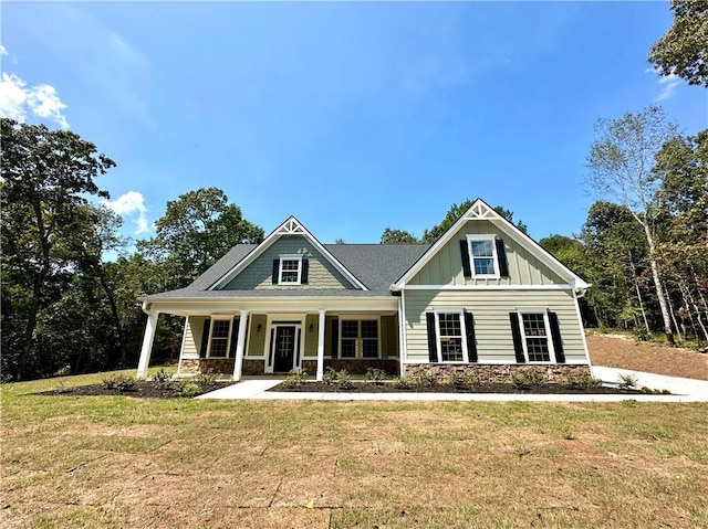 craftsman house with stone siding, a front lawn, board and batten siding, and a porch