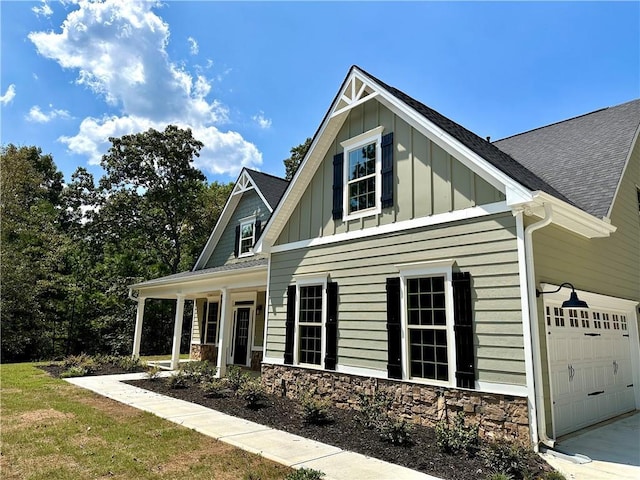 view of front facade featuring roof with shingles, a porch, board and batten siding, a garage, and stone siding