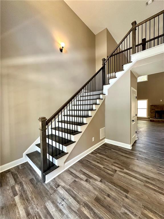 stairs with visible vents, baseboards, a towering ceiling, wood finished floors, and a stone fireplace