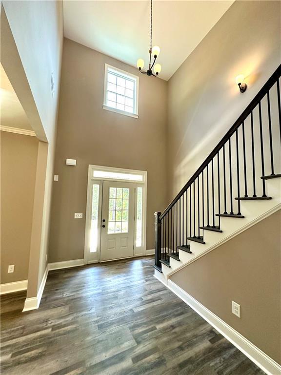 foyer featuring baseboards, dark wood finished floors, a high ceiling, stairs, and a chandelier