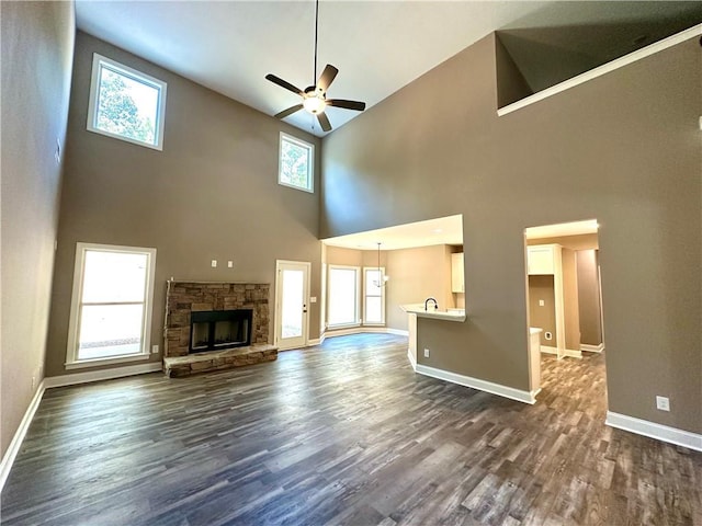 unfurnished living room with dark wood-type flooring, a healthy amount of sunlight, a stone fireplace, and a ceiling fan