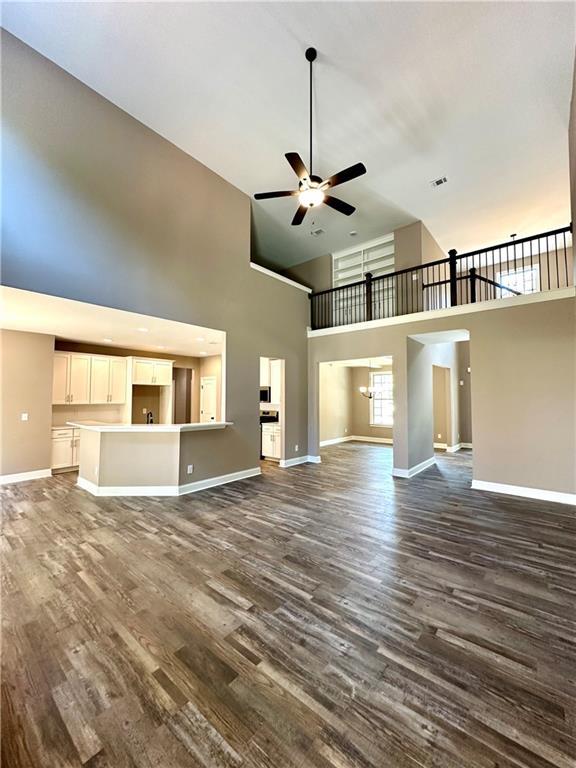 unfurnished living room with a high ceiling, dark wood finished floors, a ceiling fan, and baseboards