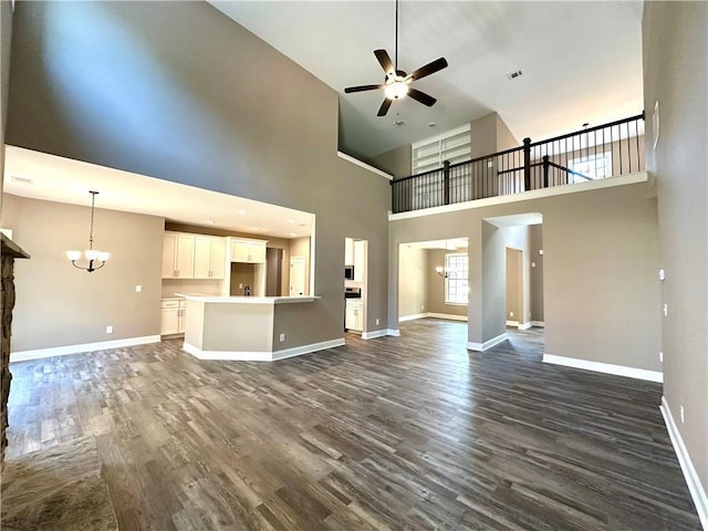 unfurnished living room with ceiling fan with notable chandelier, dark wood finished floors, visible vents, and baseboards