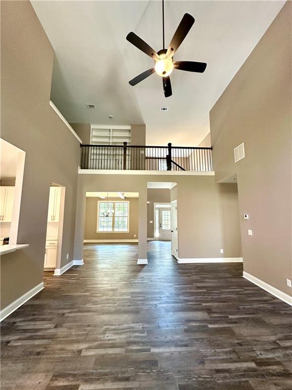 unfurnished living room with dark wood-style floors, visible vents, baseboards, and ceiling fan