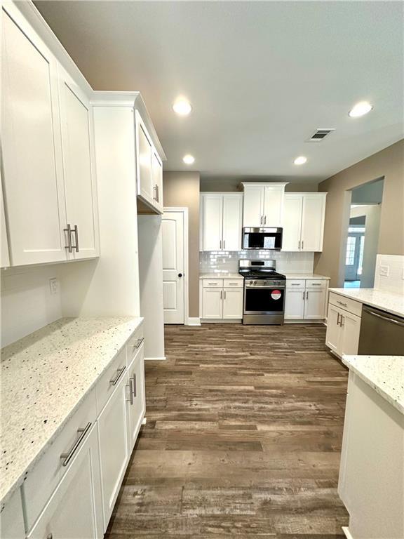 kitchen with visible vents, appliances with stainless steel finishes, white cabinets, and light stone counters