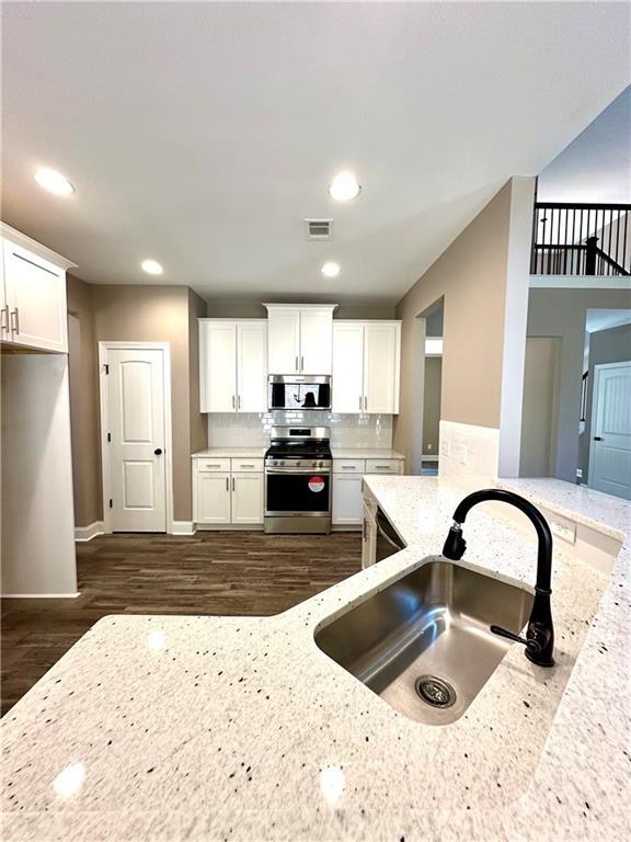 kitchen with stainless steel appliances, white cabinetry, a sink, and light stone counters