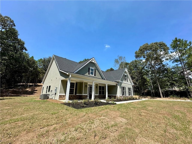 view of front of home featuring stone siding, covered porch, cooling unit, and a front yard