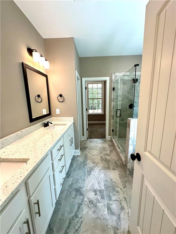 full bathroom with marble finish floor, double vanity, a sink, a shower stall, and baseboards