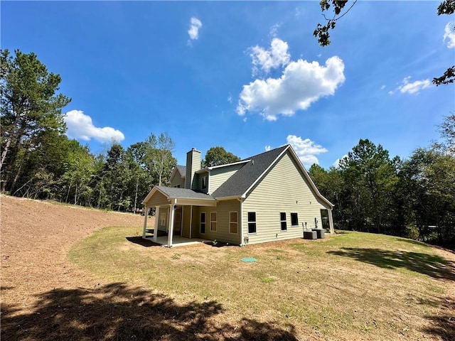 view of side of property featuring central air condition unit, roof with shingles, a lawn, a chimney, and a patio area