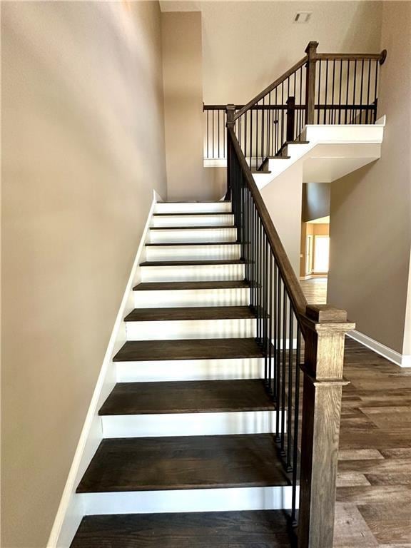 staircase with a high ceiling, wood finished floors, and baseboards