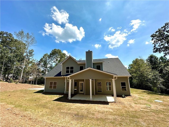 rear view of property featuring a yard, roof with shingles, a chimney, and a patio