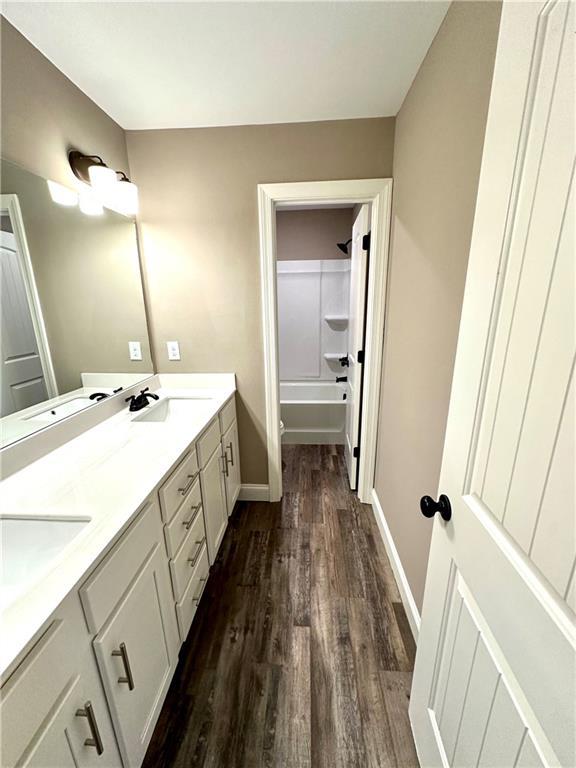 bathroom with a sink, wood finished floors, baseboards,  shower combination, and double vanity