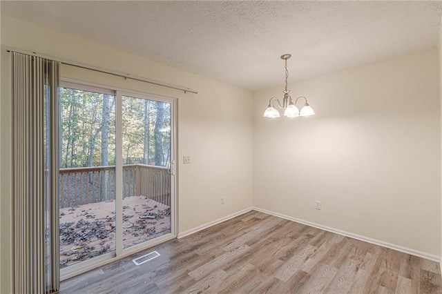 unfurnished dining area with a chandelier, a textured ceiling, and light hardwood / wood-style floors