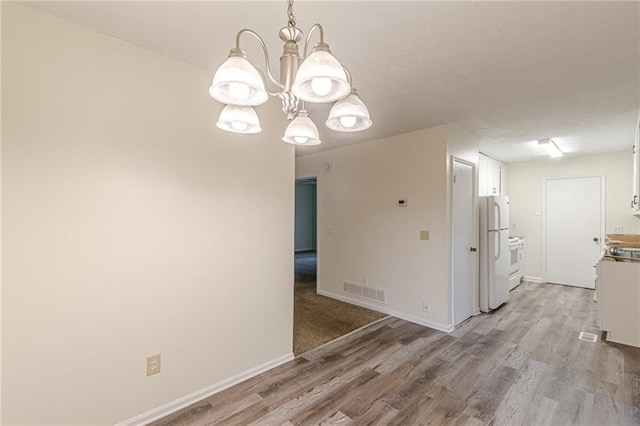 unfurnished dining area featuring light hardwood / wood-style floors and an inviting chandelier