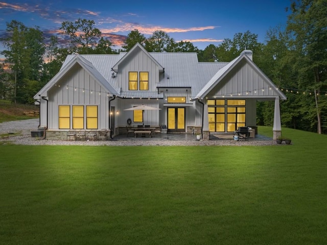 back house at dusk with central AC unit, a yard, and a patio area