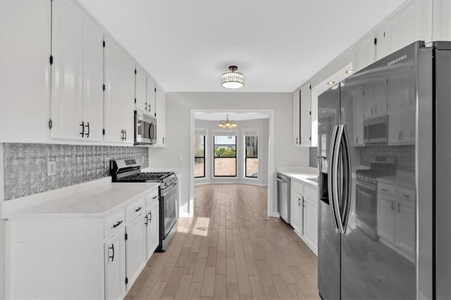 kitchen featuring light hardwood / wood-style flooring, stainless steel appliances, tasteful backsplash, white cabinets, and a chandelier