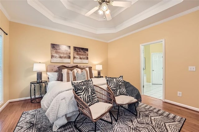 bedroom with hardwood / wood-style floors, ceiling fan, ornamental molding, and a tray ceiling