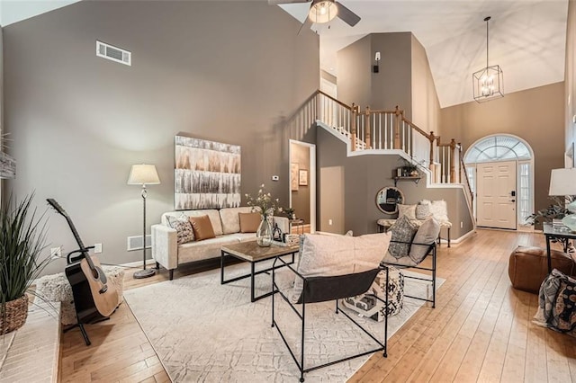 living room featuring a towering ceiling, ceiling fan with notable chandelier, and light wood-type flooring