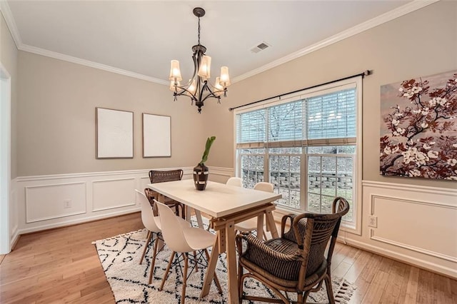 dining room with light hardwood / wood-style floors, ornamental molding, and an inviting chandelier