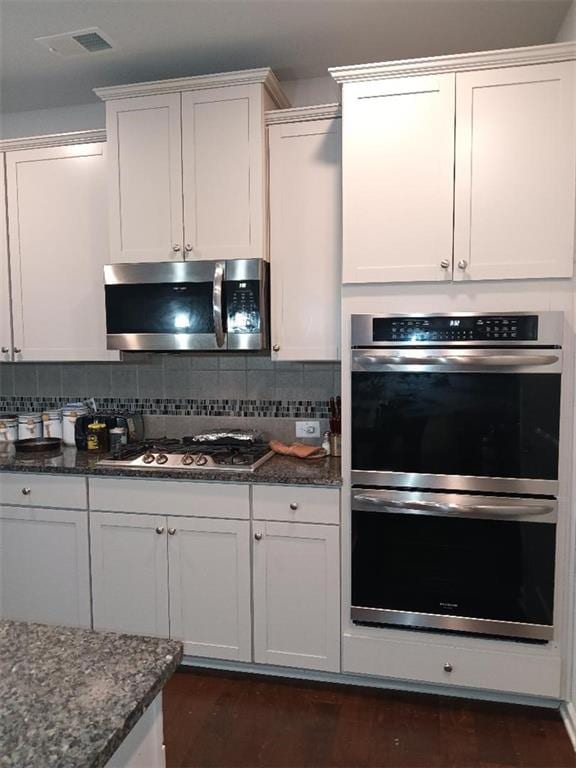 kitchen with backsplash, white cabinets, dark stone counters, and appliances with stainless steel finishes