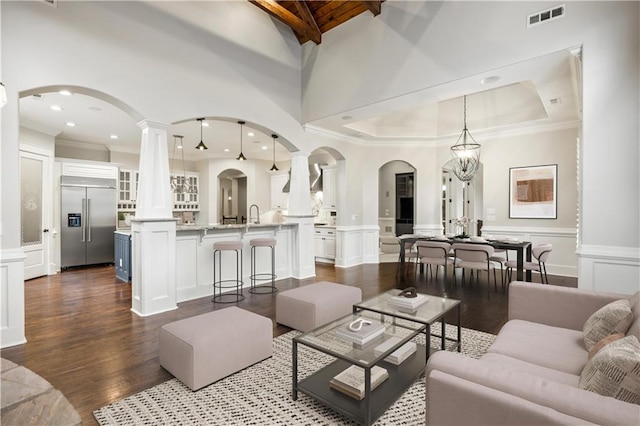 living area featuring visible vents, dark wood-style floors, arched walkways, a decorative wall, and decorative columns