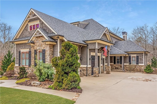 craftsman-style home featuring stone siding, a chimney, driveway, and a shingled roof