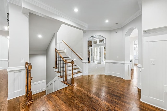 foyer featuring a decorative wall, wood finished floors, arched walkways, and ornamental molding