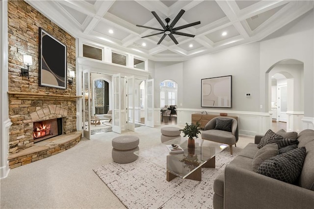 carpeted living area featuring beamed ceiling, a fireplace, a high ceiling, arched walkways, and coffered ceiling