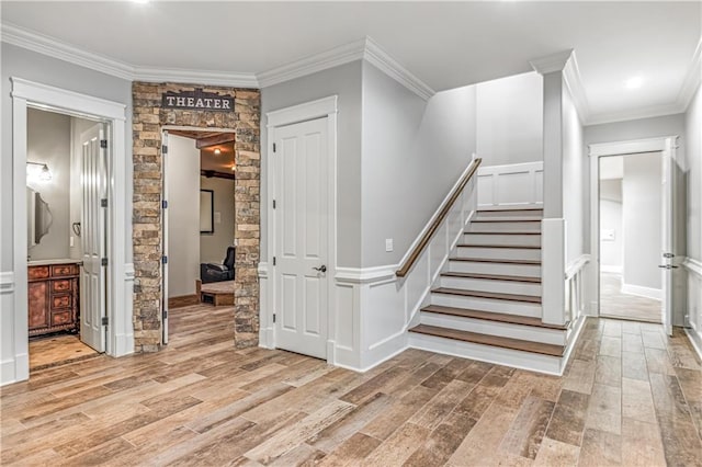 stairway with a wainscoted wall, wood finished floors, and ornamental molding