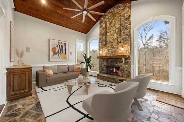 living room featuring high vaulted ceiling, stone finish flooring, a fireplace, wood ceiling, and ceiling fan