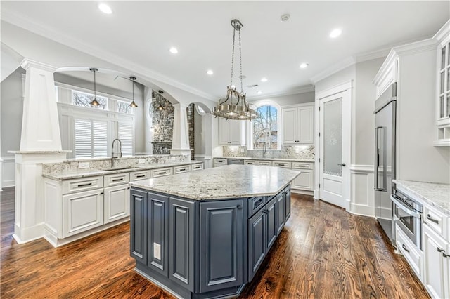 kitchen featuring a sink, dark wood finished floors, a center island, white cabinetry, and decorative columns