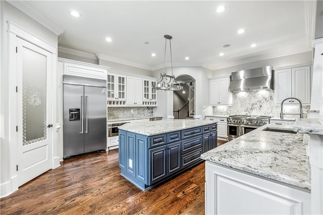 kitchen featuring high end appliances, a sink, white cabinets, wall chimney range hood, and blue cabinets