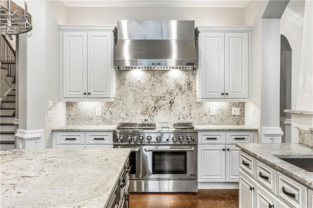 kitchen with double oven range, white cabinetry, wall chimney exhaust hood, and ornamental molding